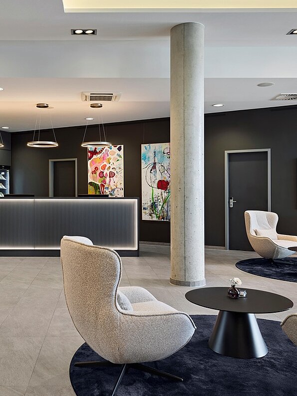 Moderne Hotellobby des Dorint Parkhotel Frankfurt Bad Vilbel mit Empfangstheke, Lounge-Sesseln, Beistelltischen, Kunstwerken und stilvollem Design in dunklen Farbtönen.